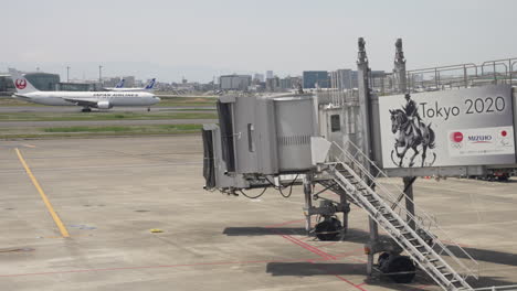 Avión-De-Japan-Airlines-Rodando-Detrás-De-Un-Puente-De-Chorro-Con-Publicidad-De-Los-Juegos-Olímpicos-De-Tokio-2020-En-Japón