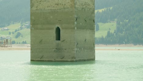Mittlere-Aufnahme,-Malerischer-Blick-Auf-Das-Fenster-Des-Kirchturms-Von-Altgraun-In-Italien,-Im-Hintergrund-Menschen-Beim-Kitesurfen