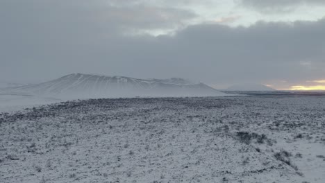 Aufsteigende-Luftaufnahme-Des-Majestätischen-Hverfjall-Kraters,-Der-Während-Eines-Mystischen-Nebligen-Tages-Mit-Eis-Und-Schnee-Bedeckt-Ist