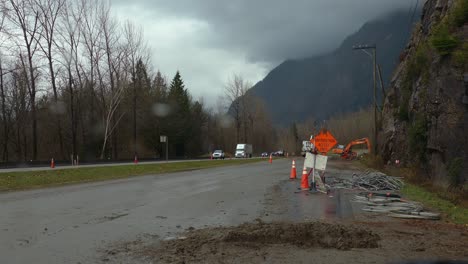 Construction-equipment,-orange-cones-and-road-signs-on-the-side-of-the-road,-during-rainfall