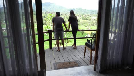 husband-and-wife-and-a-dog-enjoying-the-beauty-of-rice-fields-and-hills-from-a-villa,-Karangasem,-Bali,-October-13,-2021