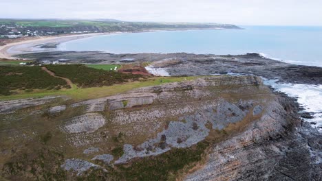 AERIAL:-Pan-out-revealing-rocky-coastline-and-curved-beach,-Port-Eynon,-Gower,-4k-Drone