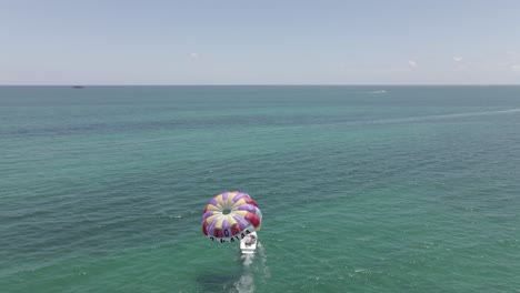 Aerial:-Tourism-boat-retrieves-colorful-parasail-in-calm,-flat-ocean