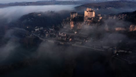 Beautiful-cinematic-aerial-view-of-Beynac-castel-above-the-fog-and-river-in-sunrise-light,-Dordogne-France,-blue-mood