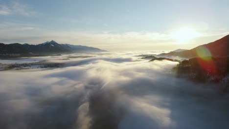 Drone-shot-of-an-incredible-landscape-covered-under-the-fog-with-surrounding-mountains-in-the-morning-at-winter-time-in-Slovenia-captured-in-4k,-drone-going-forward