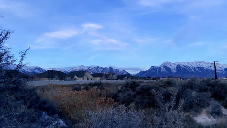 Small,-rugged-canyon-on-the-edge-of-a-suburban-neighborhood-with-snow-capped-mountains-looking-over-the-valley-community---panning-time-lapse