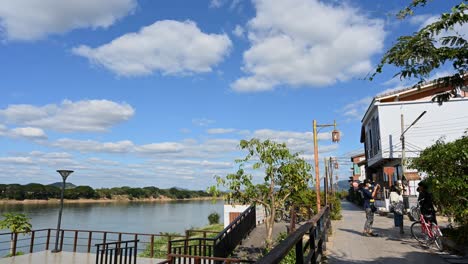 Some-people-taking-turns-in-taking-pictures-while-the-sky-is-blue-and-clouds-are-moving-captured-in-a-time-lapse,-Walking-Street,-Chiang-Khan,-Loei-in-Thailand
