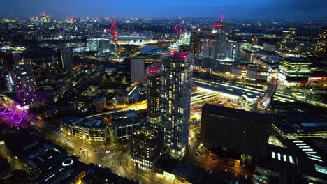 Futuristic-Stratford-illuminated-night-time-luxury-downtown-high-rise-buildings-aerial-view-dolly-right