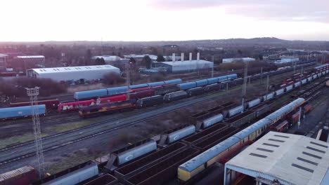 Sunrise-aerial-view-of-long-railroad-tracks-with-heavy-diesel-locomotive-carriages-and-cargo-container-yard-pull-away-shot