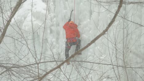 Person-climbing-ice-waterfall-during-snowfall,-view-trough-branches,-Niagara-Escapment