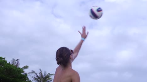 Tanned-Caucasian-woman-wearing-colorful-bikini-hits-volley-during-unisex-beach-side-volleyball-competition-filmed-in-slow-motion-from-back-side