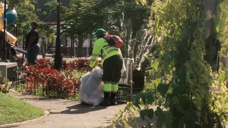 A-female-public-worker-of-the-Sanitations-Authority-of-Panama-City,-preoccupied-while-tying-a-knot-in-a-plastic-bag-of-the-trash-bin-she-has-just-emptied-in-a-park,-Causeway-of-Amador,-Panama-City