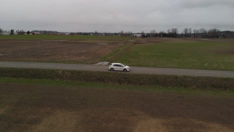 white-car-2019-toyota-corolla-hatchback-driving-along-country-farm-road-surrounded-by-grass-brown-fields-mountains-in-farmland-Abbotsford-BC-wide-Aerial-side-profile-tracking-as-car-accelerates