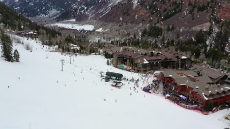 Skiing-resort-with-buildings-and-many-people-on-snowy-day,-aerial-ascend-view