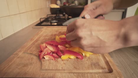 Person-Chopping-Red-And-Yellow-Peppers-On-Wooden-Board-At-Home