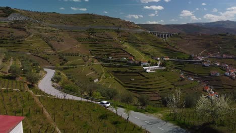 Vuelo-De-Drones-Que-Sigue-A-Un-Automóvil-Por-Un-Camino-Sinuoso-Entre-Las-Montañas-Del-Norte-De-Portugal-Y-Los-Campos-De-Vino