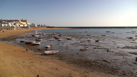 People-exploring-beach-at-low-tide-with-small-fishing-boats-in-water