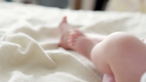 Closeup-of-joyful-baby-newborn-feet-playing-on-bedsheets,-handheld,-day