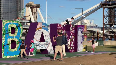 Child-climbing-up-the-iconic-landmark,-colorful-giant-block-letter-of-Brisbane-City-with-cross-river-bridge-construction-in-the-background-on-a-sunny-day,-Queensland-the-sunshine-state,-Australia