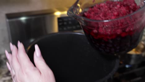 Dumping-a-bowl-full-of-raspberries-and-blueberries-into-a-pot-on-the-stove-to-make-jam---slow-motion
