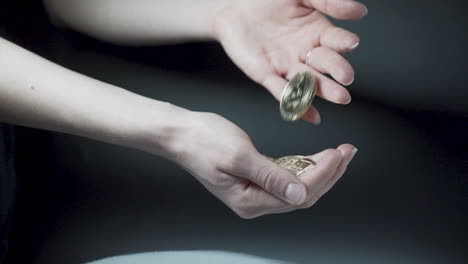 Dropping-Bitcoin-coins-from-one-hand-to-another,-black-background