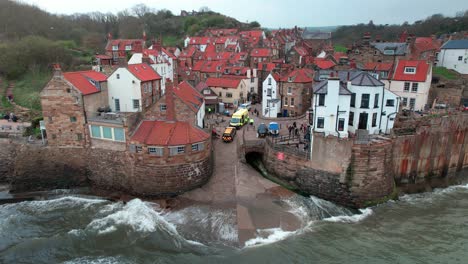 Waves-crashing-against-colourful-Robin's-hood-bay-town-houses-static-aerial-view-close-up