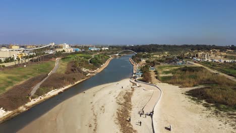 Hadera-Park-flying-in-over-river-mouth,-sandbank-and-modern-bridge-to-the-Hadera-Water-Park,-located-between-Givat-Olga-and-the-power-plant