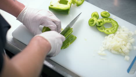 Chef-thinly-slices-green-bell-pepper-on-cutting-board,-slow-motion-top-down-4K