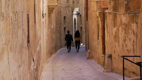 Women-friends-walking-down-narrow-passage-street-of-Mdina,-capital-of-Malta
