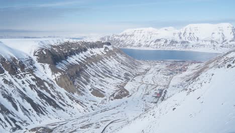 Majestic-snowy-valley-with-icy-lake-in-horizon-in-Svalbard,-aerial-view