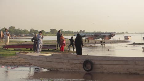 Menschen-Stehen-An-Einem-Boot-Am-Ufer-Des-Flusses-Ravi,-Im-Hintergrund-Slums