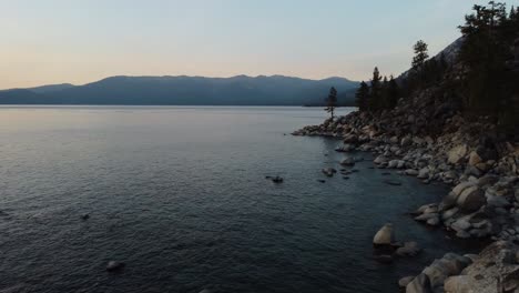 Drone-shot-flying-by-three-people-sitting-on-the-huge,-smooth-rocks-on-the-East-shore-of-Lake-Tahoe-during-sunset
