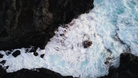 Top-down-steady-drone-footage-of-waves-rushing-between-cooled-lava-rocks