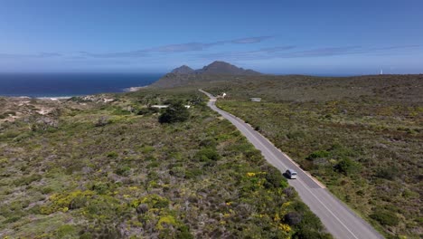 Toma-Aérea-De-Drones-De-Una-Furgoneta-Conduciendo-A-Lo-Largo-De-Una-Hermosa-Carretera-Costera-En-El-Parque-Nacional-De-Cape-Point-En-Ciudad-Del-Cabo