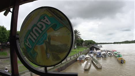 Boats-docked-along-the-riverside-behind-a-weathered-Aguila-beer-sign