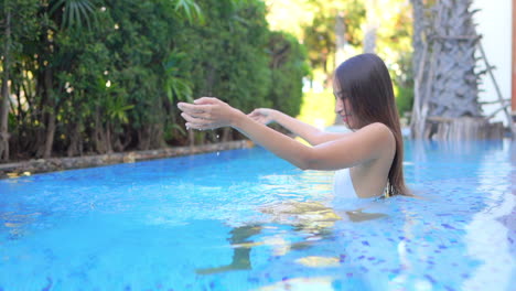 Sexy-Exotic-Woman-in-Swimsuit-Having-Fun-With-Water-in-Swimming-Pool-of-Tropical-Resort,-Slow-Motion