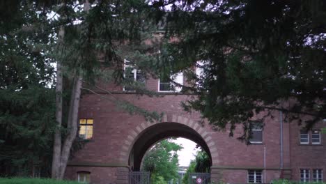 Slow-Horizontal-Motion-of-a-Dark-Brick-Building-Entrance-behind-Pine-Trees-in-a-Park