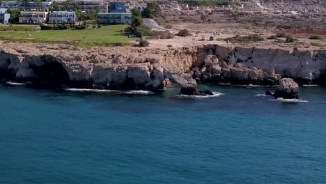 Aerial-drone-shot-of-a-rocky-sea-coast-with-a-tourist-resort-in-the-background