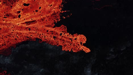 New-molten-lava-river-flowing-slowly-over-dark-basalt-rock,-top-down