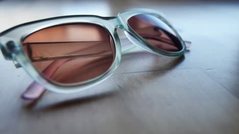 Eine-Transparente-Blaue-Sonnenbrille-Wird-Auf-Einen-Tisch-Aus-Hellem-Holz-Gestellt
