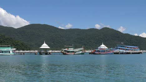Toma-Panorámica-En-Cámara-Lenta-De-Un-Muelle-Largo-Con-Muchos-Barcos-Coloridos-En-La-Isla-De-Koh-Kood,-Tailandia