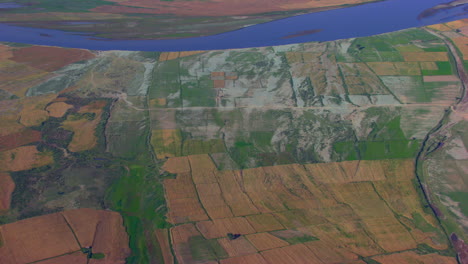 Luftaufnahme-über-Das-Land-Der-Farm-Und-Einen-Blauen-Fluss,-Straßen-Und-Bäume,-Die-Sich-In-Den-Handgefertigten-Farmen-Verteilen