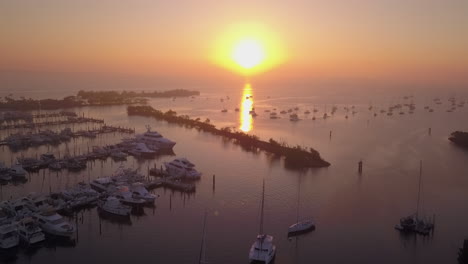 Aerial-high-angle-fly-over-boat-filled-harbor-away-from-sunrise