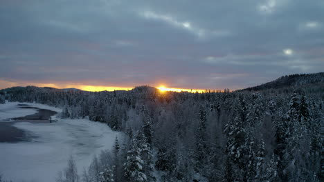 Aerial-view-across-scenic-golden-sunrise-over-frozen-Lapland-woodland-mountains