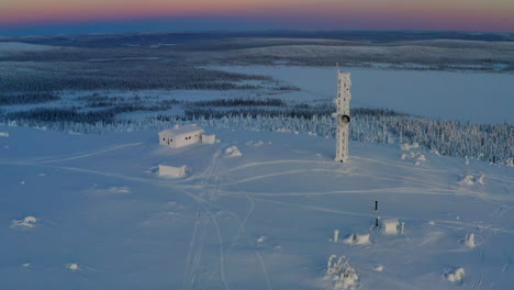 Aerial-view-orbiting-snow-covered-Lapland-remote-cabin-and-communications-tower-rising-above-polar-wilderness
