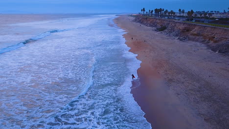 Surfer-walking-on-an-empty-beach-just-before-sunset
