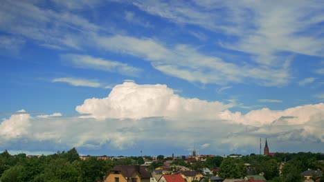 Time-lapse-of-beautiful-white-fast-moving-puffy-cumulus-clouds-on-a-sunny-summer-day,-cityscape-with-rooftops,-distant-wide-shot