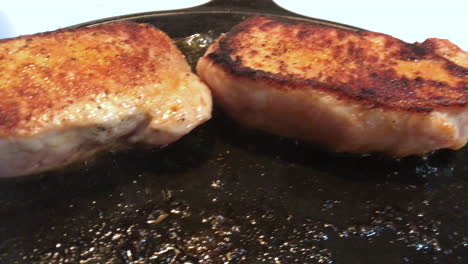 Closeup-of-delicious-looking-pork-chops-frying-in-a-cast-iron-pan-at-high-heat