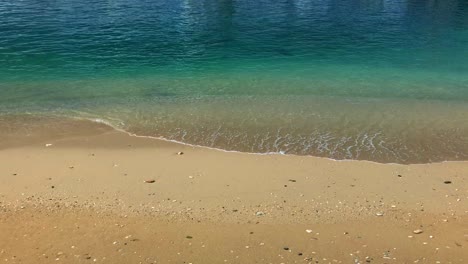 Das-Aquablaue-Wasser-Dieses-Ruhigen-Strandes,-Während-Die-Wellen-Das-Sandige-Ufer-Umspülen