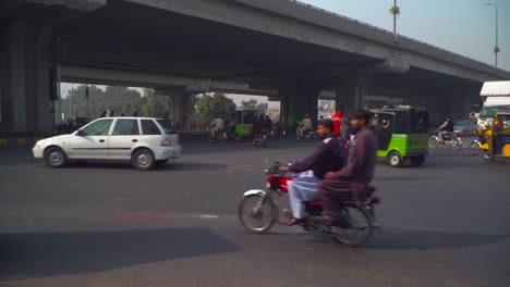 Time-laps-of-Traffic-and-people-crossing-road-on-the-square-under-the-fly-over,-An-ambulance-coming,-Rickshaws,-trucks,-motor-bikes-stopping-over-the-zebra-crossing,-streets-lights-on-the-fly-over